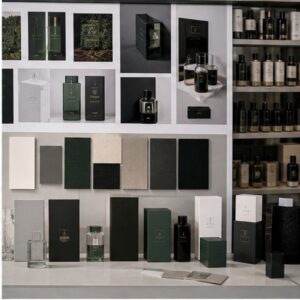Premium cosmetics packaging showroom featuring dark green and black rigid boxes, monogrammed cartons, material swatches and finished fragrance bottles